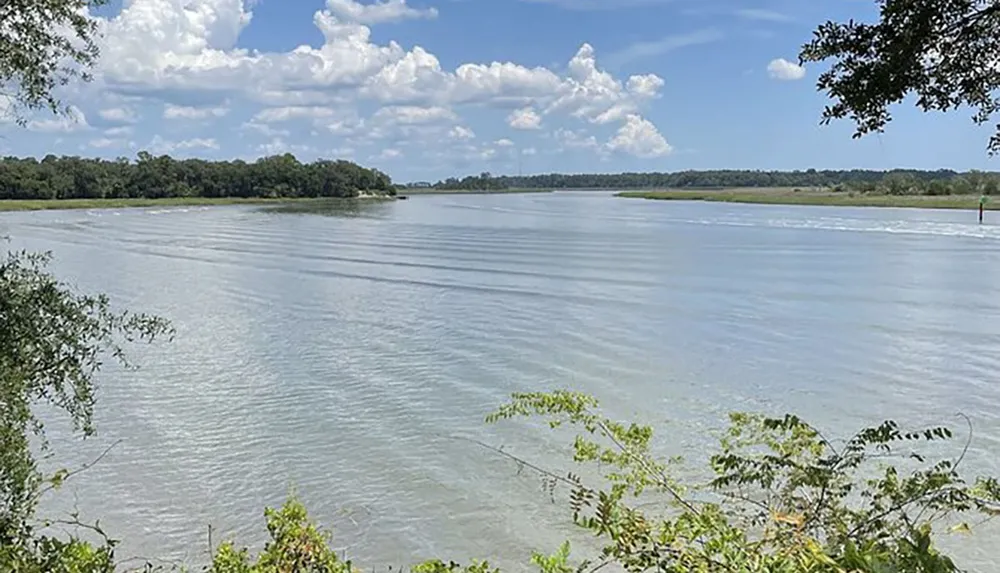 The image captures a serene riverscape with calm waters verdant riverbanks and a partly cloudy sky