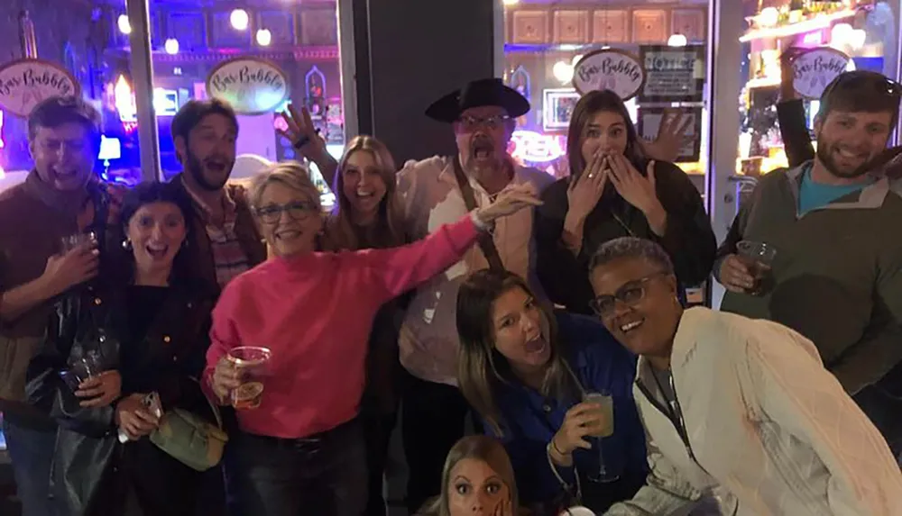 A diverse group of people pose with playful and surprised expressions for a photo in a bar or party setting