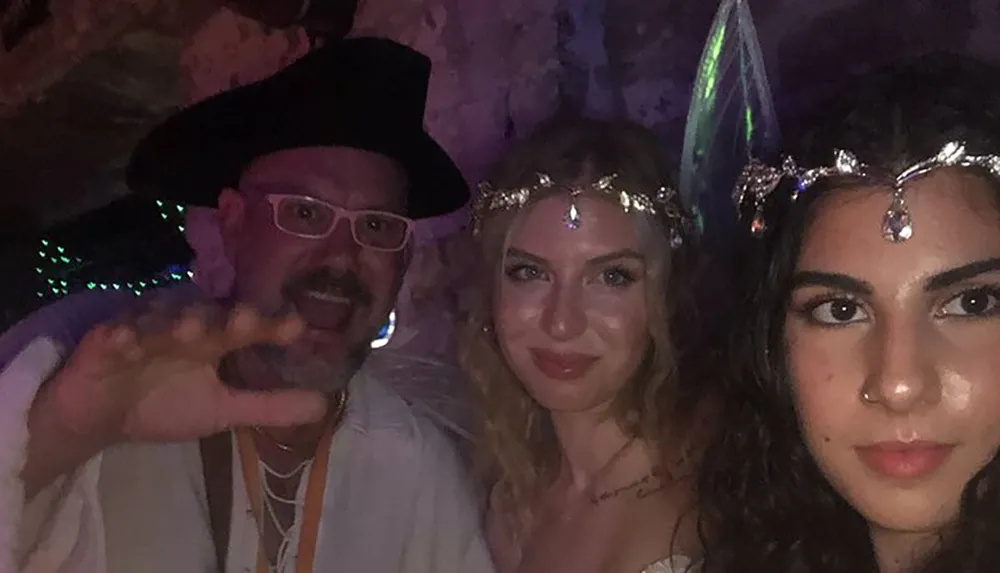 This image shows three people two women adorned with gemstone headpieces and a man wearing a pirate hat seemingly enjoying a festive or costume event