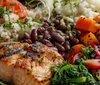 A group of individuals is engaged in conversation at an event with one smiling woman in focus and theres an inset image of a healthy plated meal