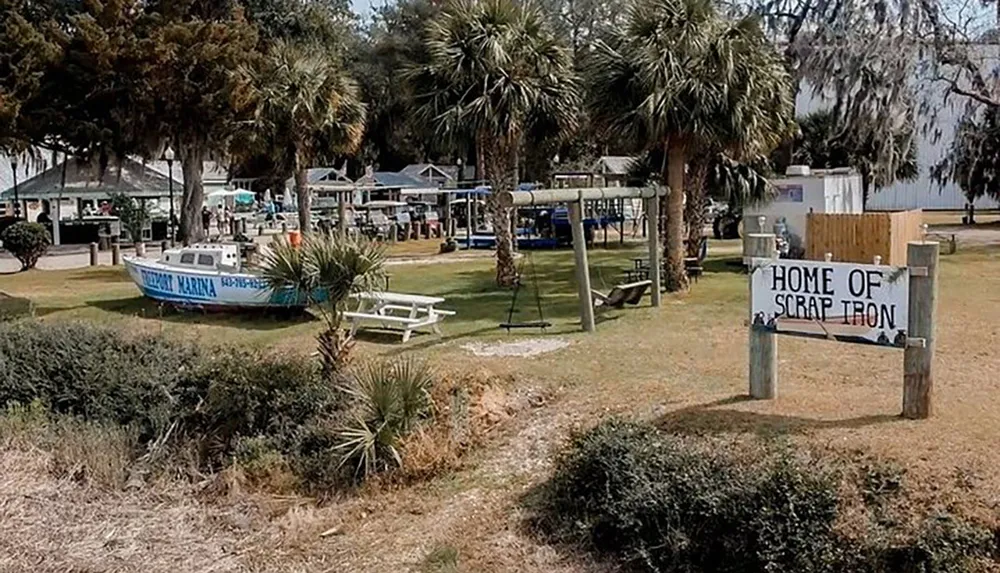 An outdoor area with a boat sign reading HOME OF SCRAP IRON playground equipment and palm trees gives a sense of a coastal recreation or community space