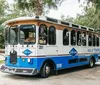 A trolley-style tour bus with the branding of Gray Line and Kelly Tours is parked near some trees