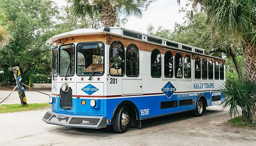 A trolley-style tour bus with the branding of Gray Line and Kelly Tours is parked near some trees