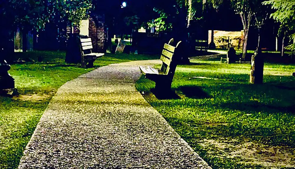 A nighttime scene of a serene park pathway lined with empty benches under the glow of streetlights