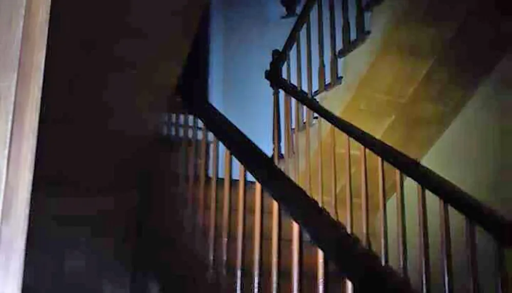 This image shows a dimly lit staircase with a wooden banister casting a shadow on the wall creating a somewhat eerie atmosphere