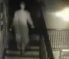 The image is a blurry and low-resolution photo of an indistinct figure standing on a staircase giving it an eerie or ghostly appearance