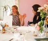 A group of people are engaged in a creative workshop painting and crafting at a table decorated with colorful art supplies flowers and drinks