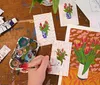 A group of people are engaged in a creative workshop painting and crafting at a table decorated with colorful art supplies flowers and drinks