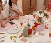 A group of people are engaged in a creative workshop painting and crafting at a table decorated with colorful art supplies flowers and drinks