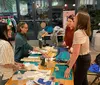 A group of people appears to be engaged in a craft or sewing workshop surrounded by fabric and sewing materials inside a well-lit room