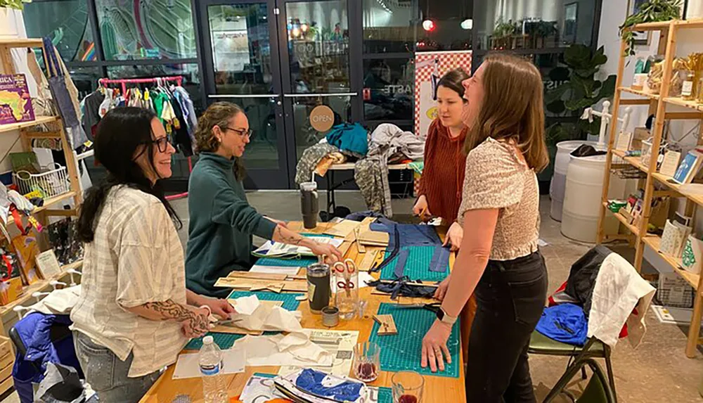 A group of people appears to be engaged in a craft or sewing workshop surrounded by fabric and sewing materials inside a well-lit room