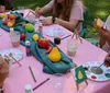 A group of people is enjoying a cheerful outdoor craft activity around a table covered in art supplies