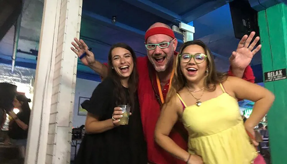 Three people are smiling and waving at the camera during a festive event