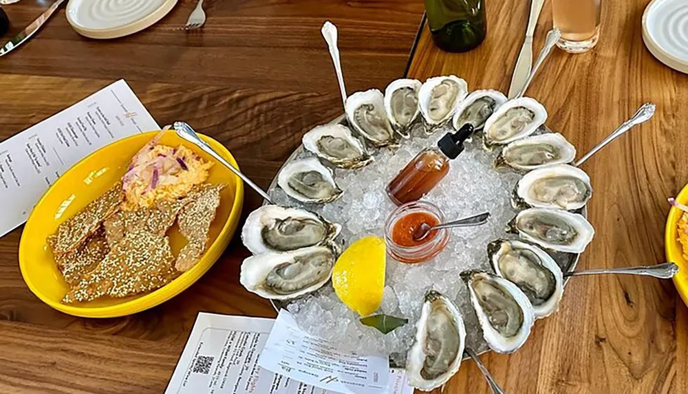 The image shows a dish of fresh oysters on ice accompanied by lemon sauces and a side dish presented on a wooden table with menus suggesting a restaurant setting