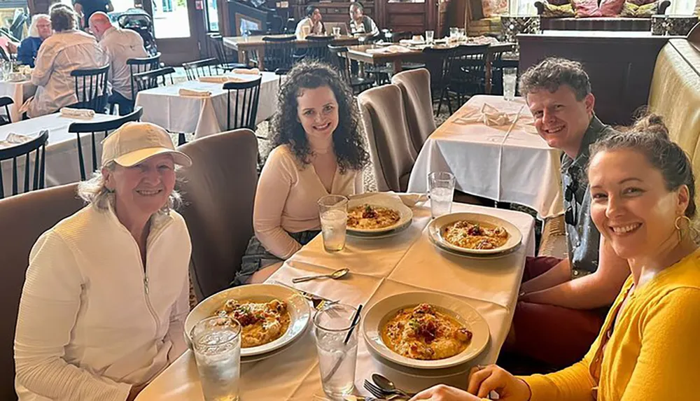 Four people are smiling at a restaurant table with plates of food in front of them