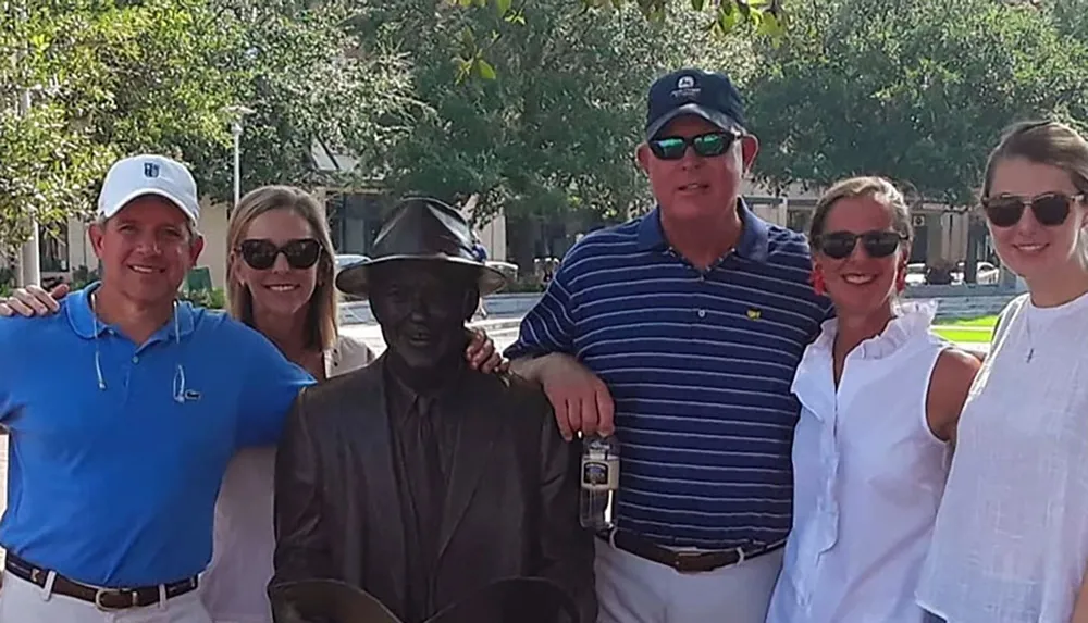 A group of four people are posing for a photo with a life-sized statue of a seated man wearing a hat