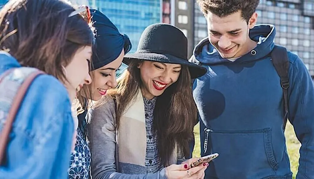 A group of young friends is smiling and looking at a smartphone together outdoors