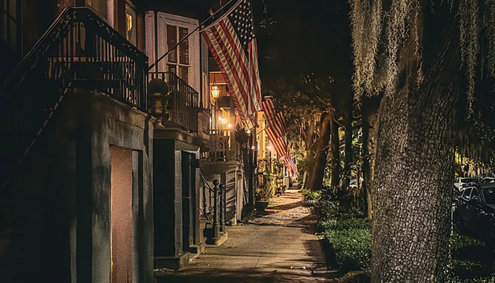 The image displays a charming nocturnal street view adorned with American flags hanging from traditional buildings illuminated by warm streetlights and lined with trees draped in Spanish moss