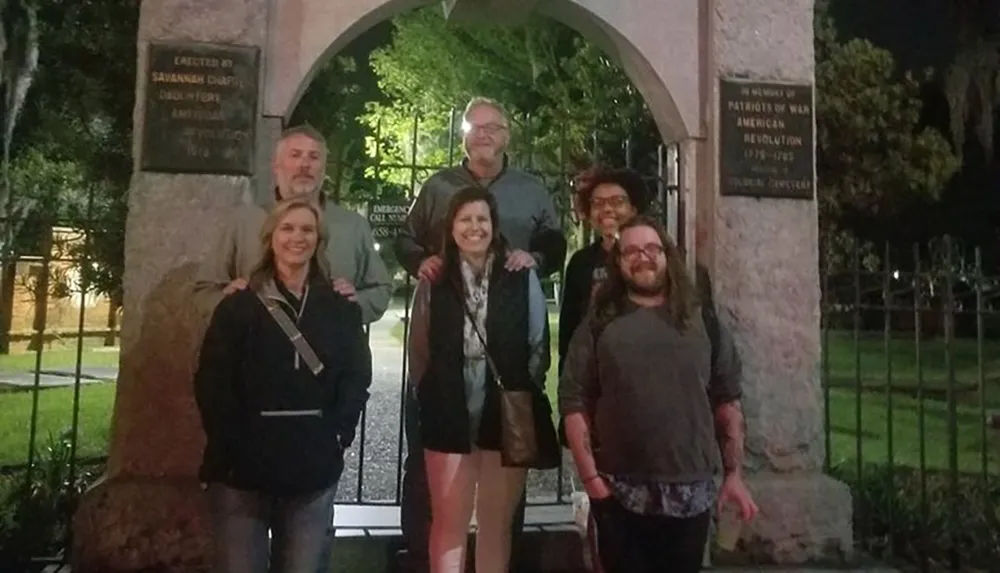 A group of six people are posing for a photo at night in front of a historical monument with plaques