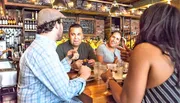 A group of people appear to be enjoying each other's company at a bar or restaurant with drinks and food on the table.
