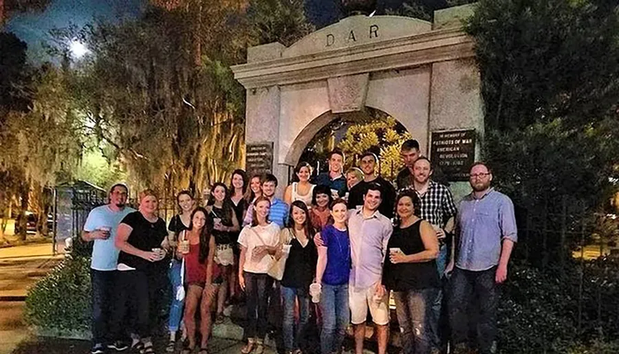 A group of people are smiling and posing for a photo at night in front of an archway that has the letters D A R on it.