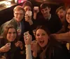 A group of smiling people are holding up their cups in a toast-like gesture seemingly enjoying a social gathering