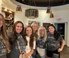 A group of women wearing matching t-shirts that say Shanias Last Swing Before the Ring are smiling for a photo in what appears to be a winery or tasting room
