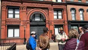 A group of people is on a guided tour outside the historic Savannah Cotton Exchange building.