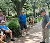 A group of people listens to a speaker in a park with lush trees and Spanish moss while others enjoy the surroundings