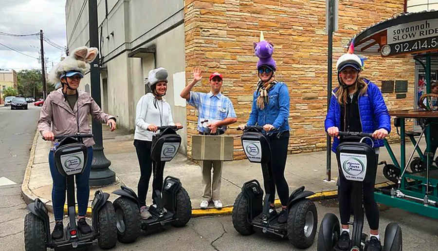 A group of people wearing whimsical hats is preparing for a Segway tour on an urban street.