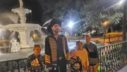 An adult dressed in a pirate costume is posing with four children by a lit fountain at night.