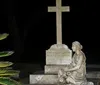 The image shows a white statue of a young girl in vintage clothing illuminated at night with a dark hedge in the background