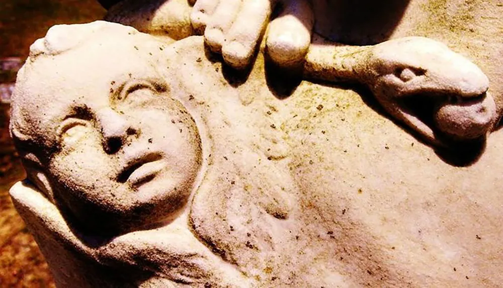 This image depicts a close-up of a weathered stone sculpture showing a distressed human face clutched by a hand