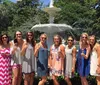 A group of smiling women pose for a photograph in front of a white fountain on a sunny day