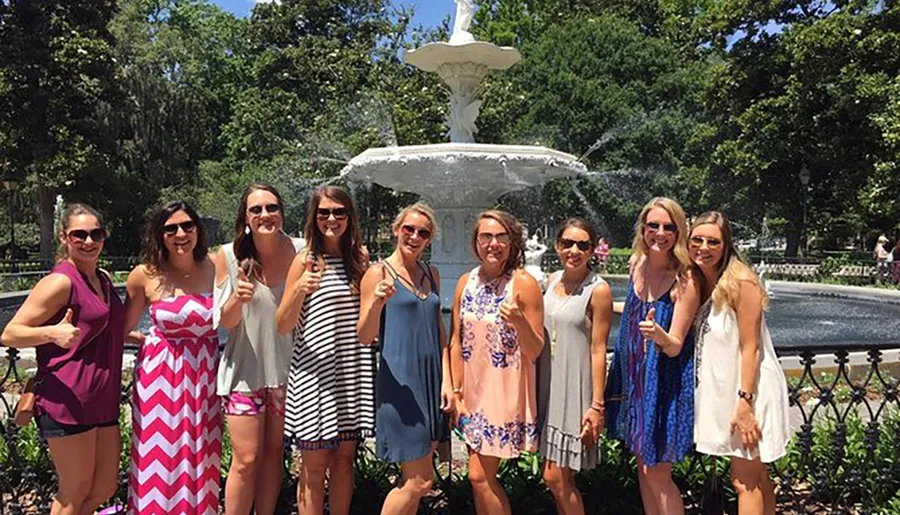 A group of smiling women pose for a photograph in front of a white fountain on a sunny day.
