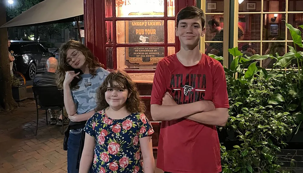 Three individuals are posing for a photo at night in front of a pub with a sign that reads Creepy Crawl Pub Tour