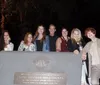A group of seven people is smiling for a photo at night in front of a historical marker commemorating the original 1733 burial plot allotted by James Edward Oglethorpe to the Savannah Jewish community