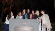 A group of seven people is smiling for a photo at night in front of a historical marker commemorating the original 1733 burial plot allotted by James Edward Oglethorpe to the Savannah Jewish community.