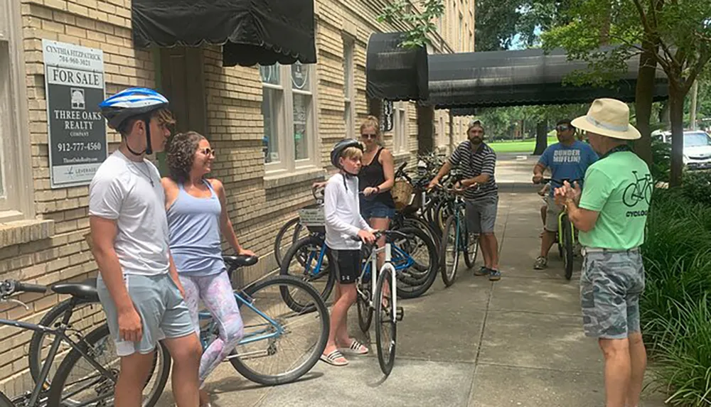 A group of people on a bicycle tour listens to a guide speaking on a sidewalk in an urban setting