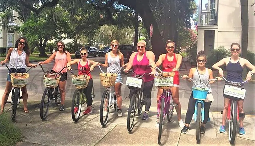 A group of eight individuals is smiling for the camera while standing with bicycles on a sunny day likely enjoying a group ride or outing