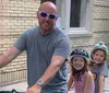 A man with two smiling children wearing helmets are preparing for a bike ride