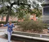 A person gestures animatedly while giving a tour or presentation in a park with benches and a monument surrounded by trees with Spanish moss