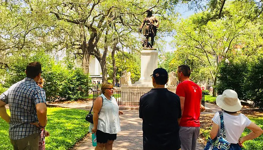 A group of people is standing in a park looking at a statue surrounded by lush greenery.
