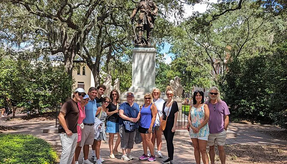 A group of people is posing for a photo in front of a statue in a park surrounded by trees