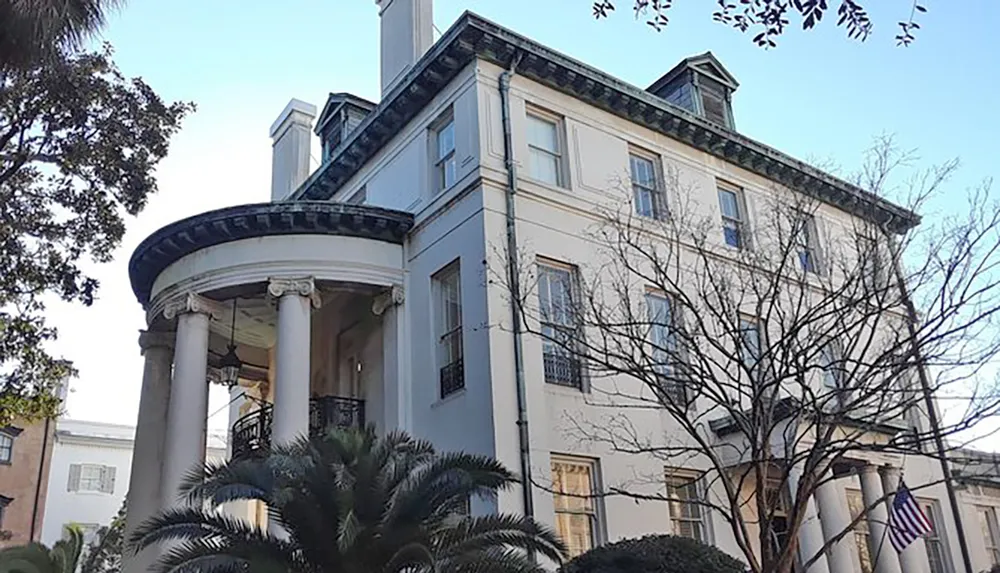 The image shows a stately historic building with a large circular portico supported by classical columns and an American flag displayed prominently in front