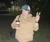A person is posing at night with a peace sign and holding a cup with a pumpkin design