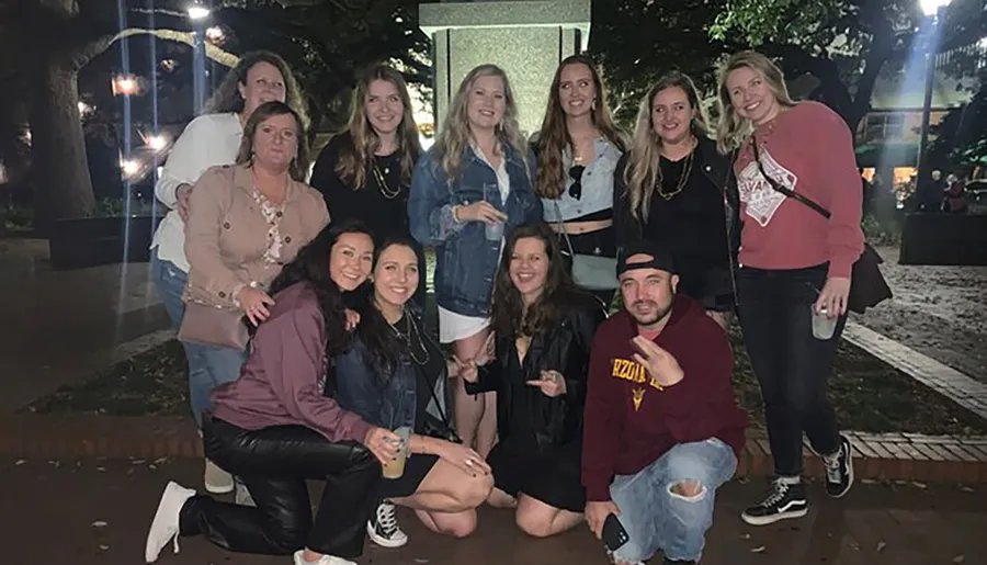 A group of people pose for a photo at an outdoor evening gathering, with some sitting and others standing, displaying a mix of casual and smiling expressions.