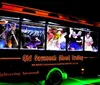 The image shows the Old Savannah Ghost Trolley tour bus at night illuminated with neon lights and featuring actors dressed as ghostly characters interacting with passengers
