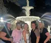 Five individuals are posing for a photo in front of a beautifully lit fountain at night