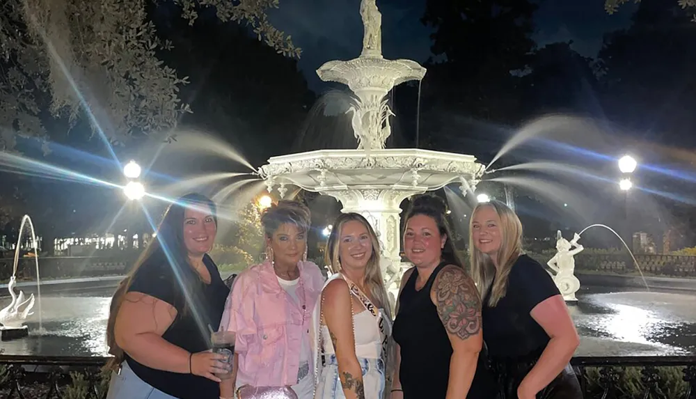 Five individuals are posing for a photo in front of a beautifully lit fountain at night